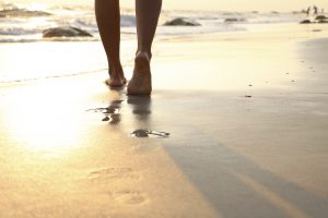 Girl walking on wet sandy beach leaving footprints